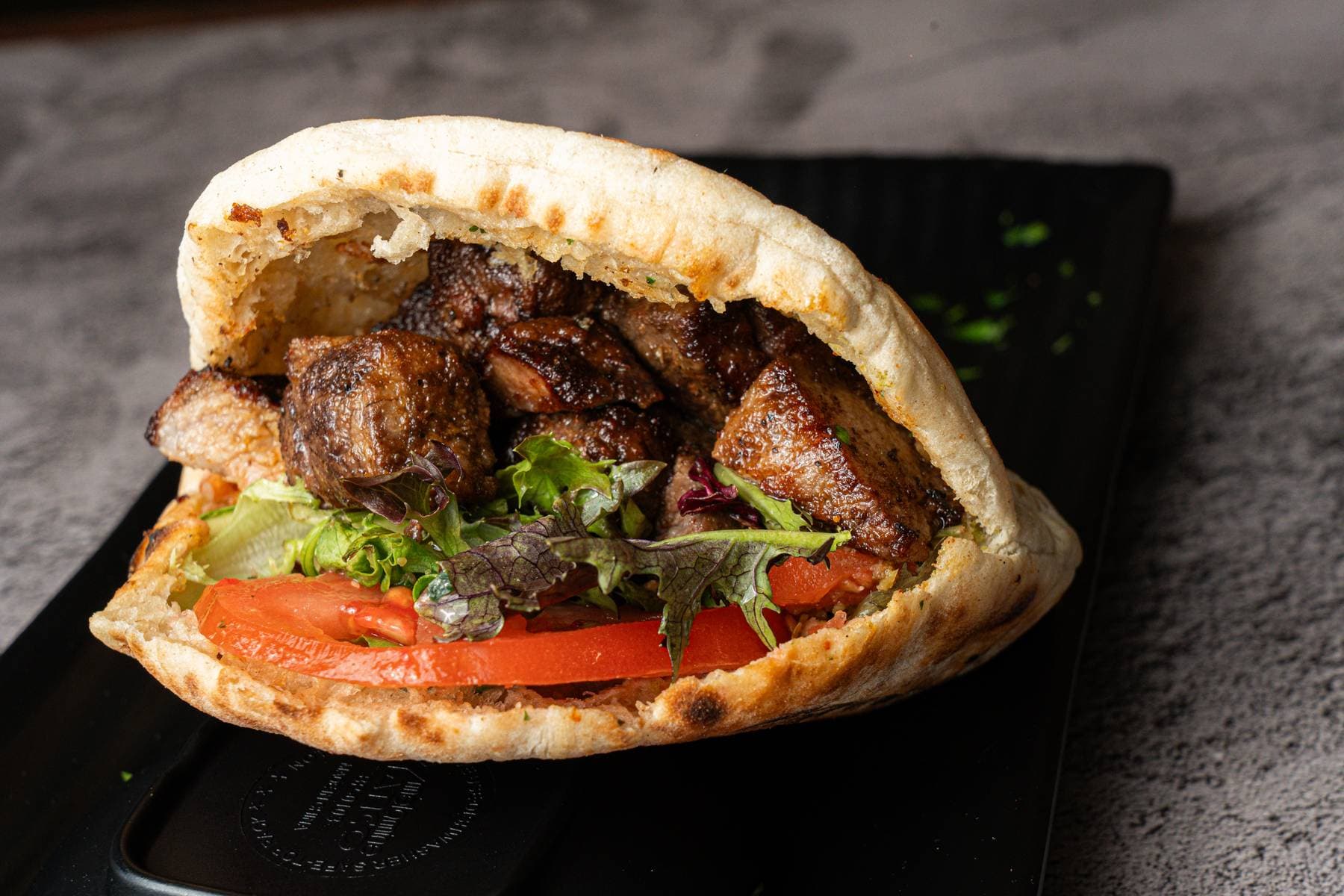 Beef shawarma stuffed into a soft pita with tomato and crisp lettuce, served on black slate