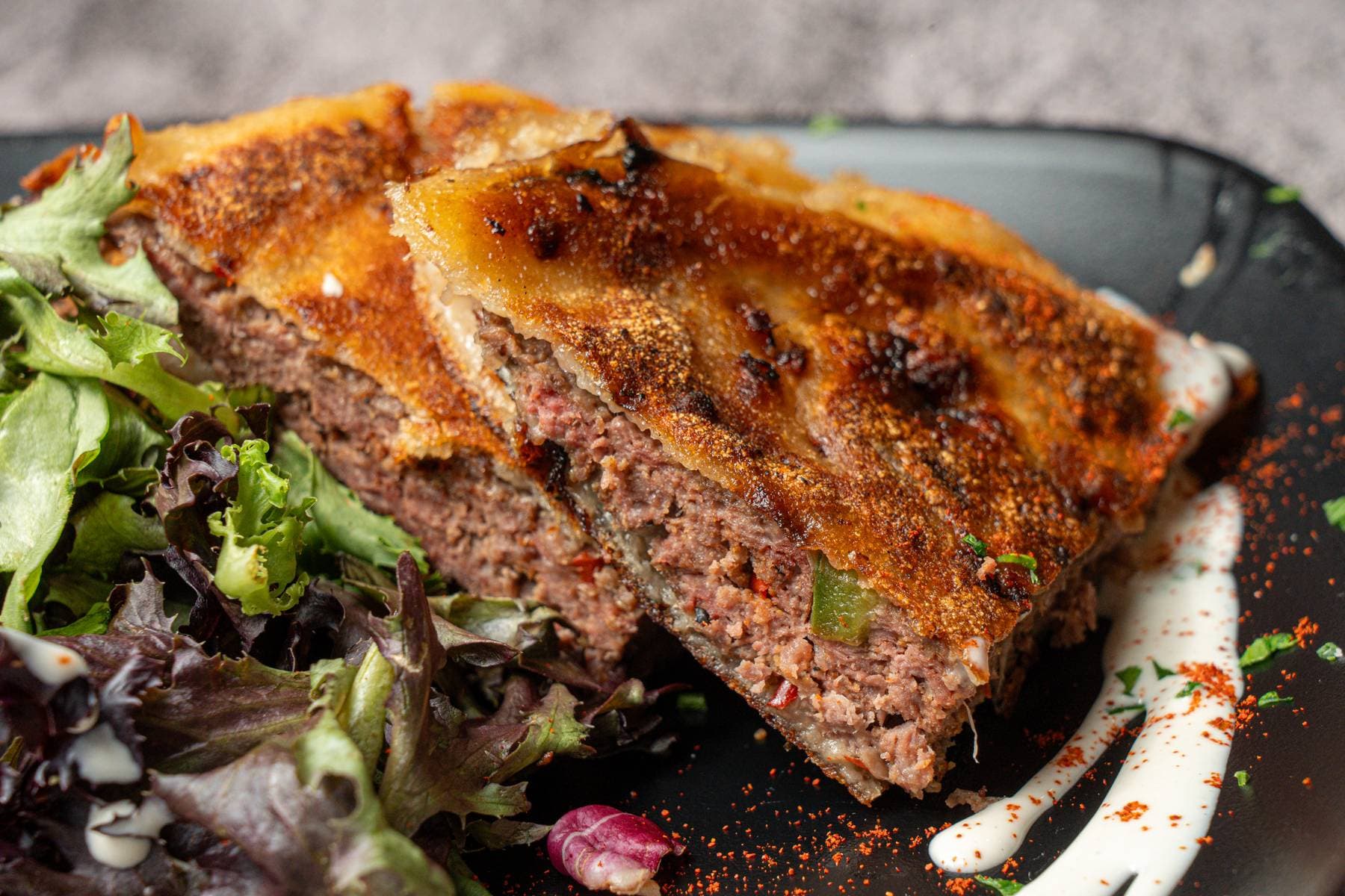 Egyptian hawashi, spiced beef baked into golden flatbread, sliced and plated with mixed greens and paprika
