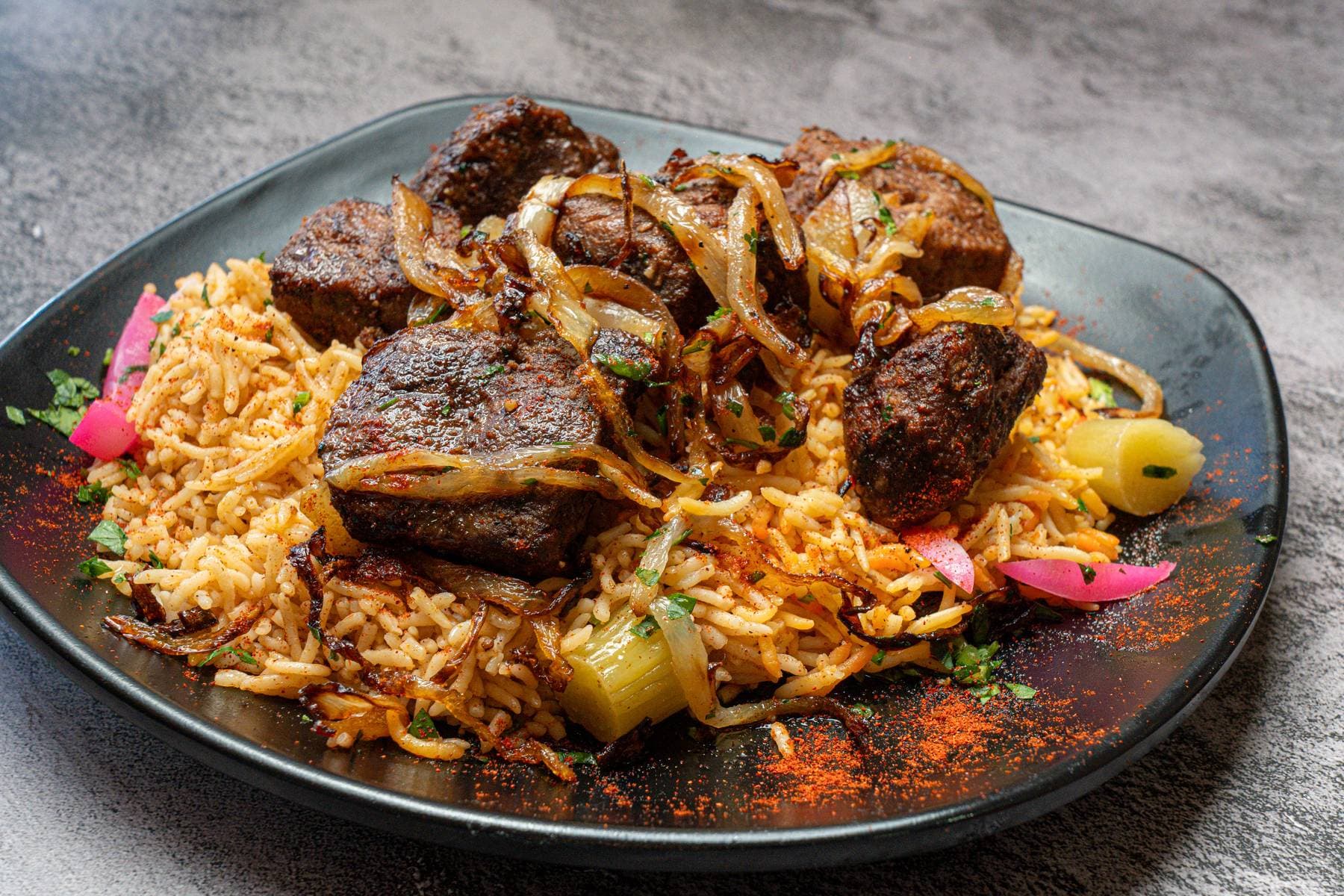 Lamb kebab platter, tender cubes piled over saffron rice with caramelized onions and pink pickled turnip