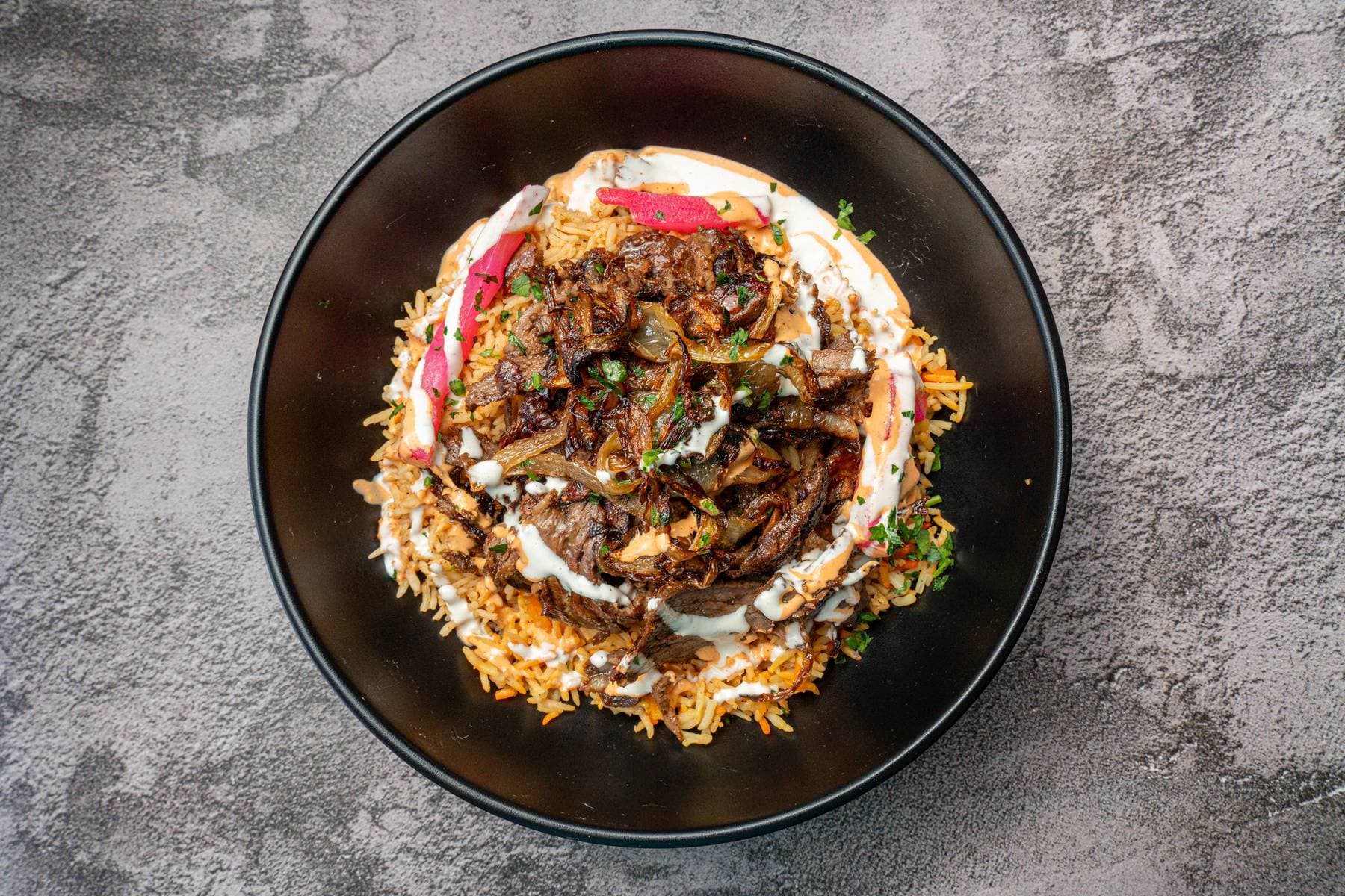 Overhead bowl of beef shawarma over Egyptian rice with tahini and pickled vegetables